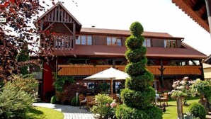 A two-story wooden building with a balcony, a garden with benches, and a well-maintained lawn. - HÔTEL À LA FERME (Osthouse)