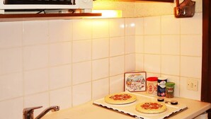Une cuisine compacte équipée d’un four à micro-ondes, d’un évier et d’un petit plan de travail sur lequel sont posées deux pizzas.