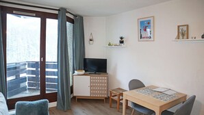 Un salon chaleureux avec une table à manger en bois, un canapé et un téléviseur posé sur un meuble.