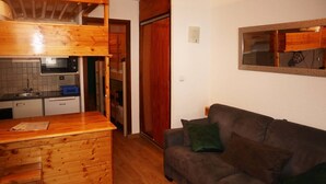 Un espacio habitable compacto con kitchenette, una barra de madera y un sofá con cojines.