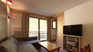 A cozy living room with a sofa, a coffee table, a TV on a wooden stand, and a sliding glass door leading to an outdoor area.