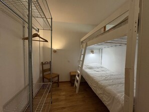 Habitación con literas, un estante metálico, una silla y una pequeña mesa.