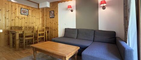 A room with a wooden dining table, chairs, a sofa, and two wall-mounted lamps.