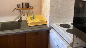A compact kitchen with wooden cabinets, a stainless steel sink, a dish rack, a dishwasher, and a stove.