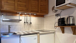 A compact kitchen with wooden cabinets, a stainless steel sink, and a built-in refrigerator. - Studio à Deux pas du Centre (LES ORRES 1650)