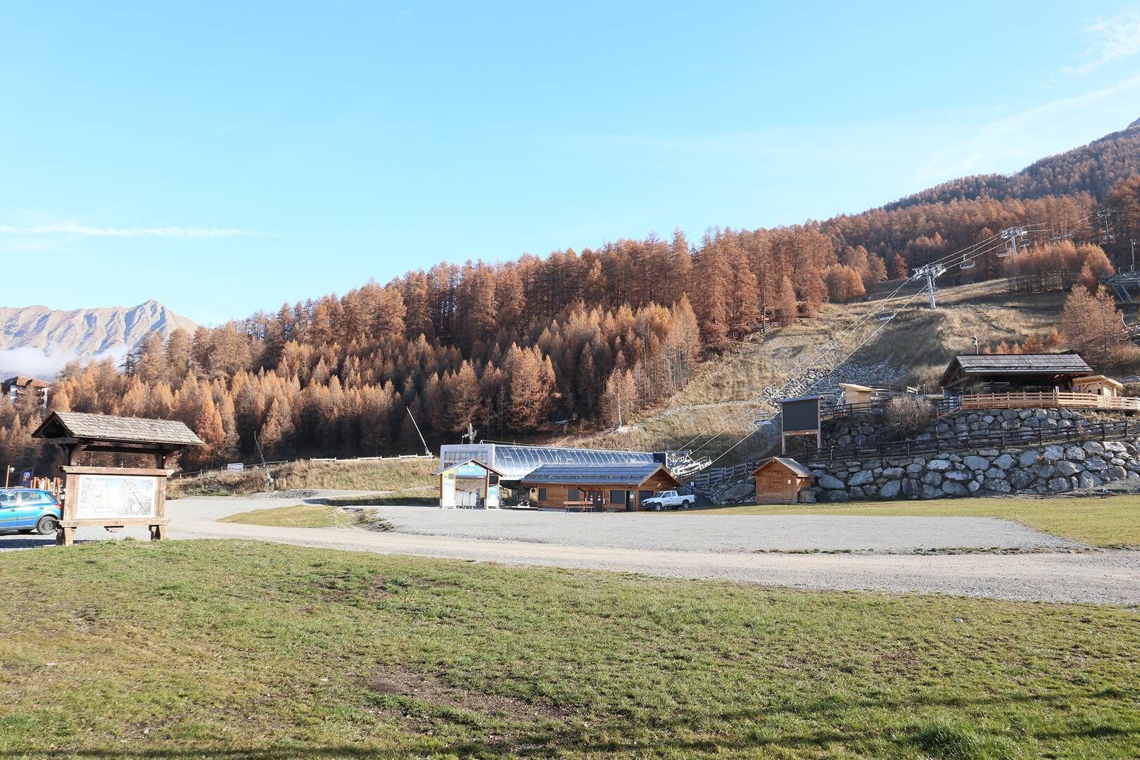 A mountain lodge with a stone wall, wooden cabins, and a ski lift in the background.