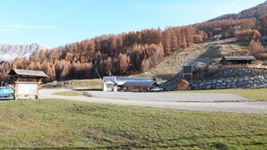 Een berghut met een stenen muur, houten chalets en een skilift op de achtergrond.