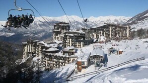 A ski resort with a cable lift, multiple buildings, and a snowy landscape. - Studio 4 Personnes vue Pistes (LES ORRES 1650)