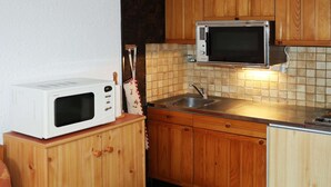 A compact kitchen with wooden cabinets, a microwave, a sink, and a tiled backsplash. - Studio 4 Personnes vue Pistes (LES ORRES 1650)