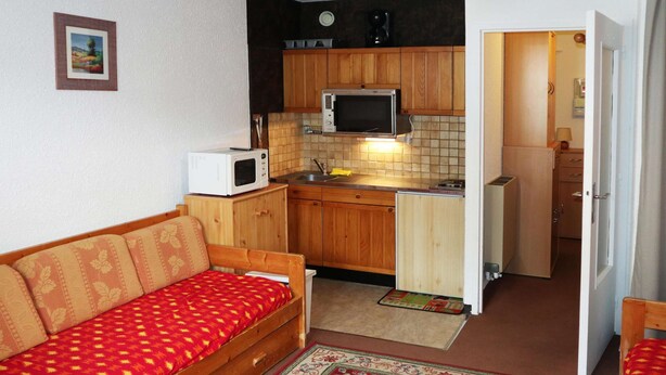 A compact living space with a kitchenette, a sofa, and a door leading to another room. - Studio 4 Personnes vue Pistes (LES ORRES 1650)