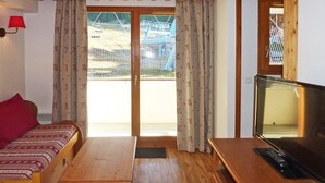 Una habitación acogedora con una cama de madera, una mesita, un televisor y un ventanal corredero que da a un espacio al aire libre.