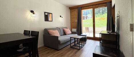 A modern living room with a sofa, a dining table, and a TV stand.
