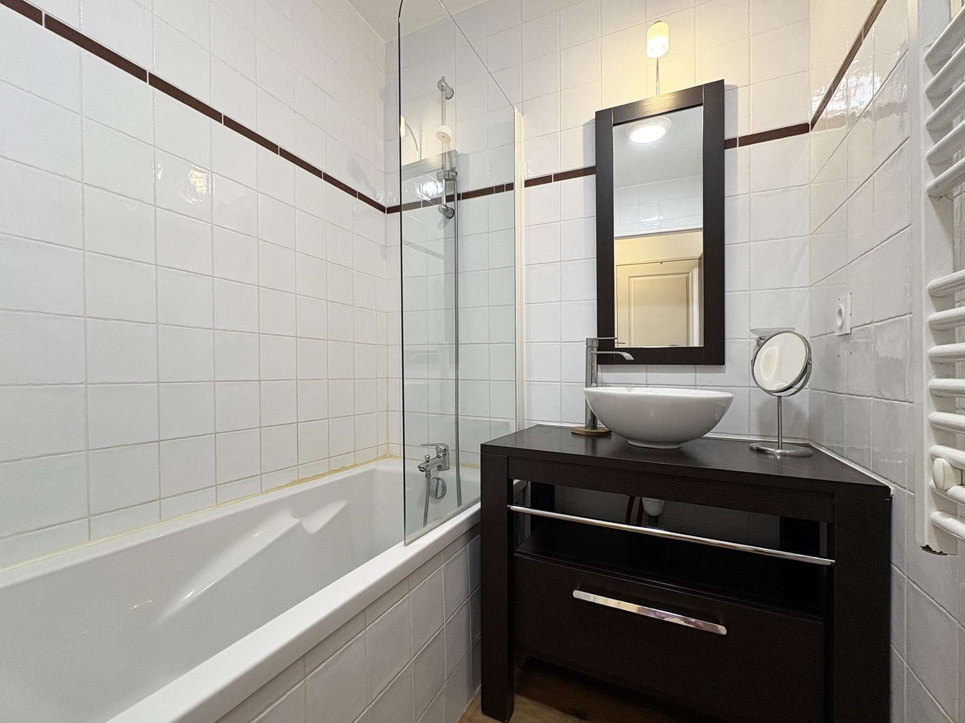 Een moderne badkamer met een douchecabine van glas, een witte badkuip en een donkere wastafel met spiegel en wasbak.