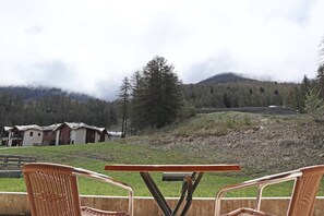 A view of a mountain landscape with a row of cabins and a table with chairs in the foreground.