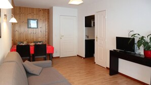 A living room with a sofa, a dining table with chairs, a TV, and a kitchen area in the background. - Apartment in luxury residence (LES ORRES 1800)