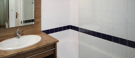 Une salle de bain avec un meuble-lavabo en bois, un lavabo blanc, un miroir et une baignoire ornée de carreaux blancs et bleu foncé.