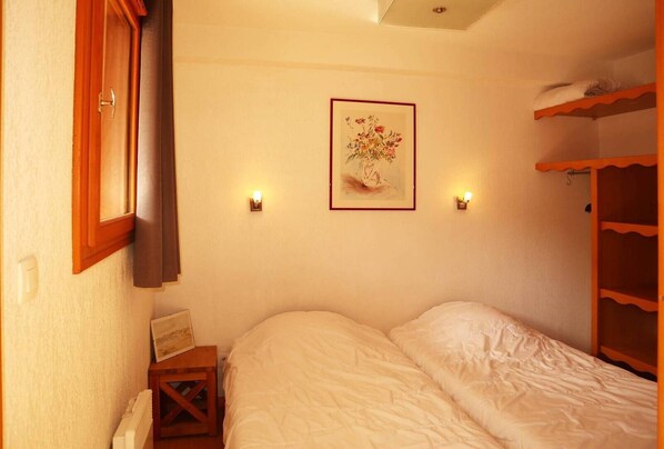 A small, cozy bedroom with a single bed, a wooden wardrobe, and a framed floral artwork on the wall. - Appartement Parc DES Airelles 211 (LES ORRES 1800)