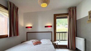 Une chambre à coucher comprenant un lit, deux lampes de chevet, une petite table et une vue sur l’extérieur par une porte.