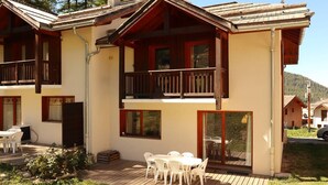 Un chalet à deux étages doté d’un balcon, d’une terrasse en bois et d’un coin repas avec mobilier d’extérieur.