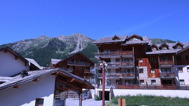 Un immeuble en bois à plusieurs étages, doté de balcons, qui se dresse sur un fond de paysage montagneux.