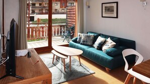 Un salon avec un meuble TV en bois, un canapé turquoise agrémenté de coussins, une petite table ronde et un balcon offrant une vue sur les immebles.