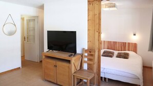 Une pièce comprenant un lit, un téléviseur posé sur un meuble en bois, une petite table et une chaise.