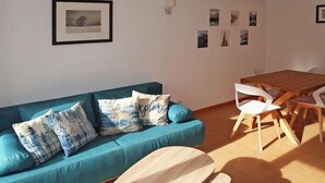 Un salon avec un canapé de couleur turquoise, des chaises blanches, une table en bois et des tableaux encadrés accrochés au mur.
