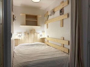 A bedroom with a wooden headboard, a bedside table, a hanging light, and a shelf above the bed.