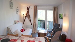 Een gezellige woonkamer met een bank, een stoel, een tafel en een balkon met gordijnen.