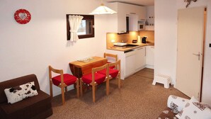 A compact living space with a kitchenette, a dining area with a table and chairs, a sofa, and a small stool. - Grand Studio 4 Personnes (LES ORRES 1650)