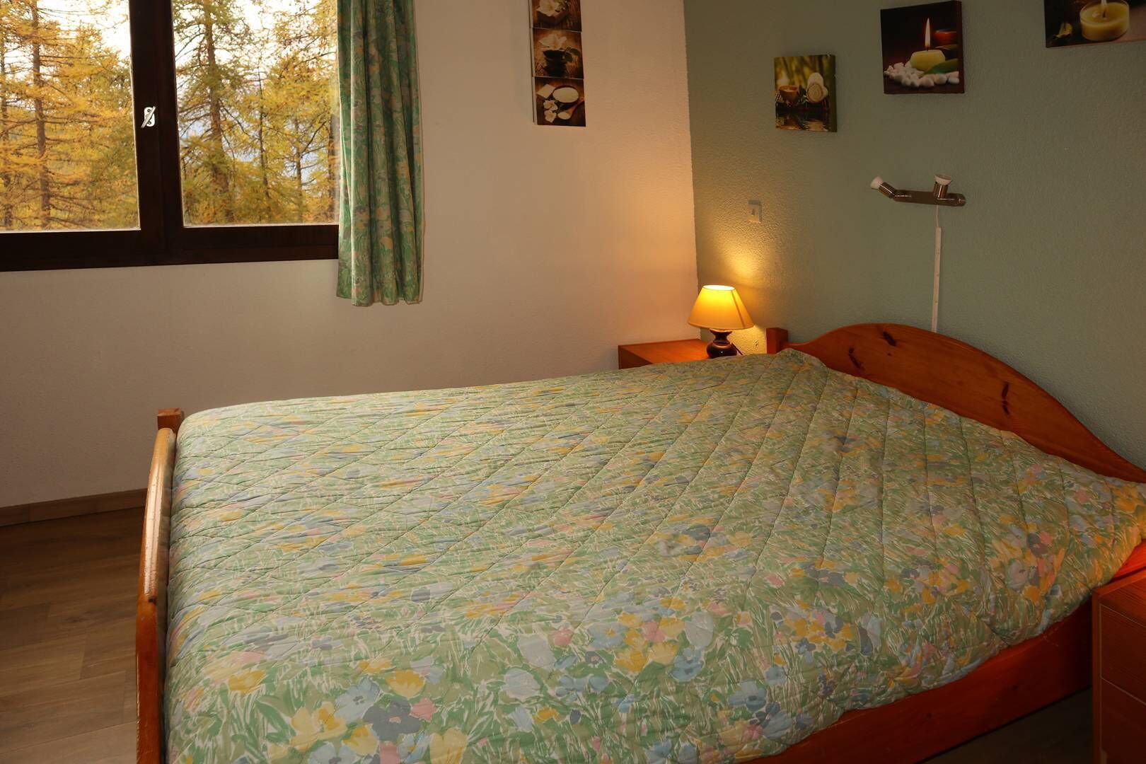 A bedroom with a bed, a nightstand, a lamp, and a window with a view of trees.