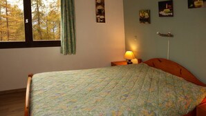Ein Schlafzimmer mit einem Bett, einem Nachttisch, einer Lampe und einem Fenster mit Blick auf Bäume.