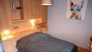 A bedroom with a bed, wooden nightstands, a desk, and a lamp.