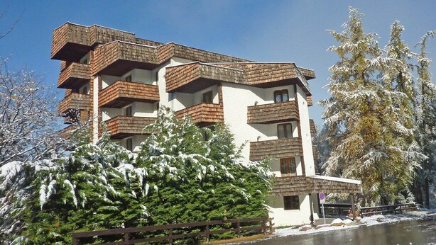 A multi-story building with balconies, surrounded by snow-covered trees.