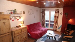 A cozy living room with a red sofa, wooden cabinets, a TV, and a balcony with curtains.
