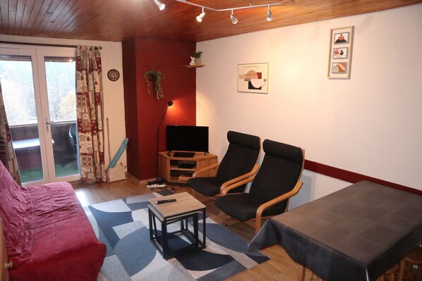 En hyggelig stue med en rød sofa, to sorte lænestole, et træbord og et TV-møbel med et fladskærms-TV.
