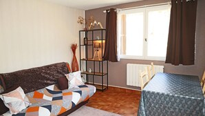 A cozy living room with a sofa, a small table, a bookshelf, and a window with curtains. - Studio N° 213 LES Flocons (LES ORRES 1650)