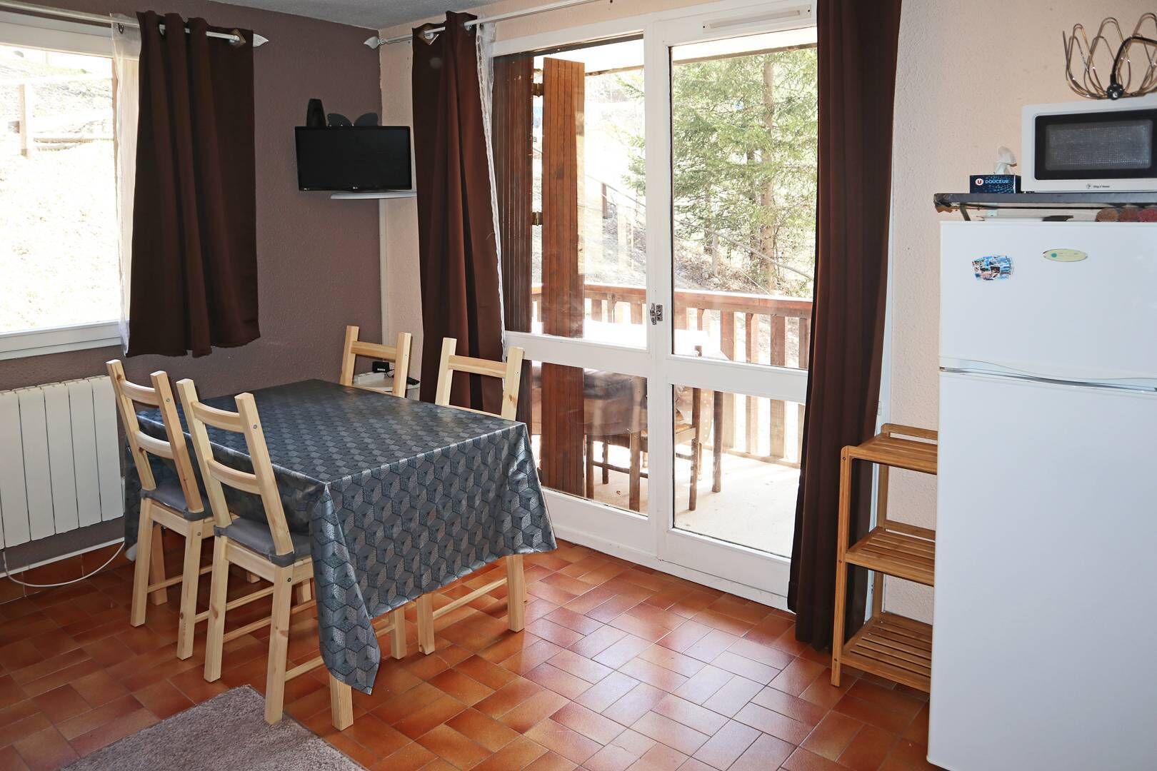 Een eetruimte met een tafel en stoelen, een televisie aan de muur en een koelkast.