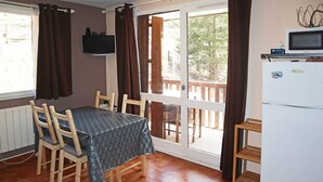 A dining area with a table and chairs, a television on the wall, and a refrigerator. - Studio N° 213 LES Flocons (LES ORRES 1650)