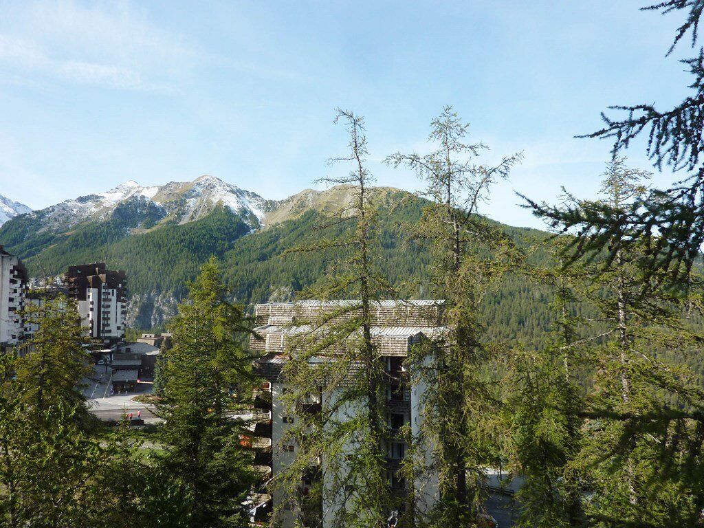 Un paese di montagna con un edificio dotato di cortile centrale, circondato da alberi e vista sulle montagne innevate.