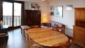 A dining area with a wooden table and chairs, a sofa, a cabinet, and a lamp. - Appartement G307 LES Cembros (LES ORRES 1650)