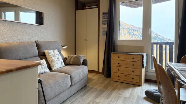 A cozy living room with a sofa, a wooden dresser, and a dining area with a table and chairs.