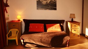 A bedroom with a bed, two bedside tables, a chair, and a wall-mounted picture. - Studio 6 Personnes Accès Direct aux Pistes (LES ORRES 1650)