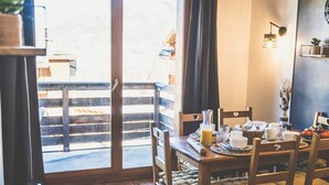 Een gezellig eetgedeelte met een houten tafel en stoelen, een televisie op een dressoir en uitzicht op een houten terras door een glazen deur.