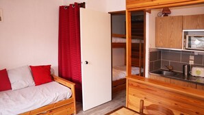 A compact room with a wooden bed, a small kitchenette, and a red curtain.