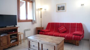 Una sala de estar con un sofá a rayas rojas, una mesa de centro de madera, un televisor sobre un mueble de madera y una lámpara de pie.