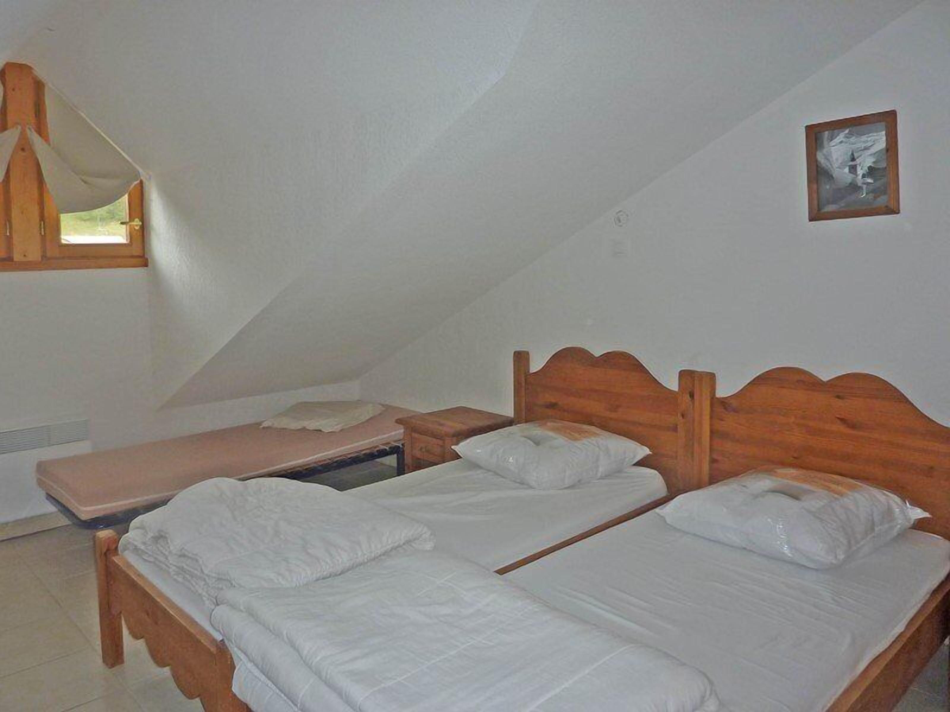 Una habitación pequeña y sencilla con dos camas de madera, una ventana con marco de madera y una mesita de noche de madera.