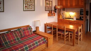 A cozy room with a wooden bed, a dining table with chairs, and a kitchen area.