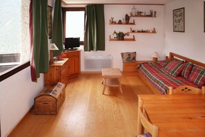 A compact room with a bed, a small table, a television, a radiator, and shelves with various items.