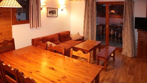 Un tavolo da pranzo in legno con sedie, un divano e una televisione in una stanza accogliente con pareti in legno e una porta scorrevole in vetro.